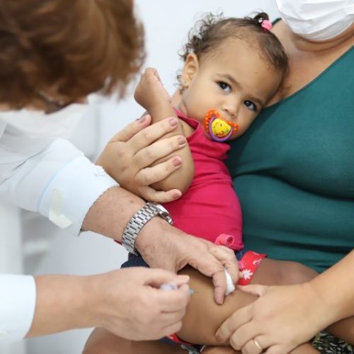 Profissional de saúde vacina na perna criança no colo da mãe
